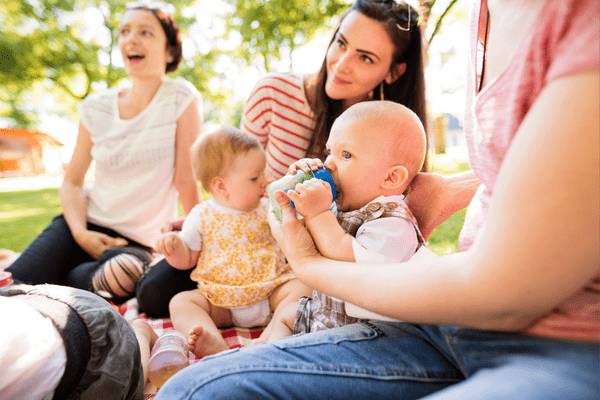 Mother feeding baby on picnic blanket.